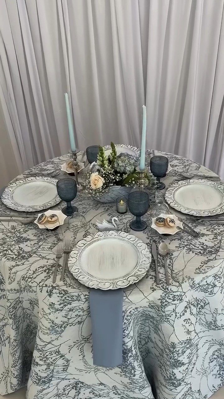 Wedding table setting with dusty blue linens, sage greenery, and white floral centerpiece.