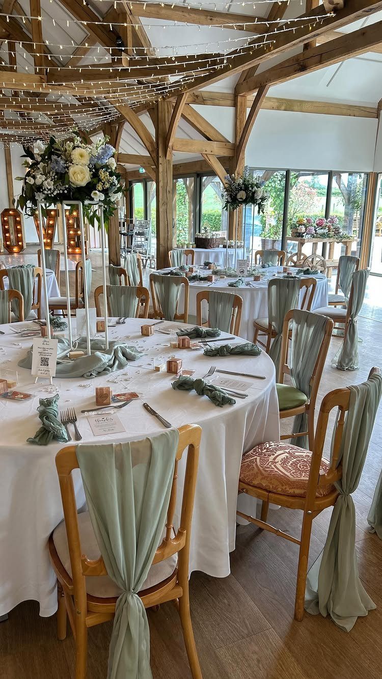 Wedding reception tables with ivory linens and sage green chair sashes in a barn