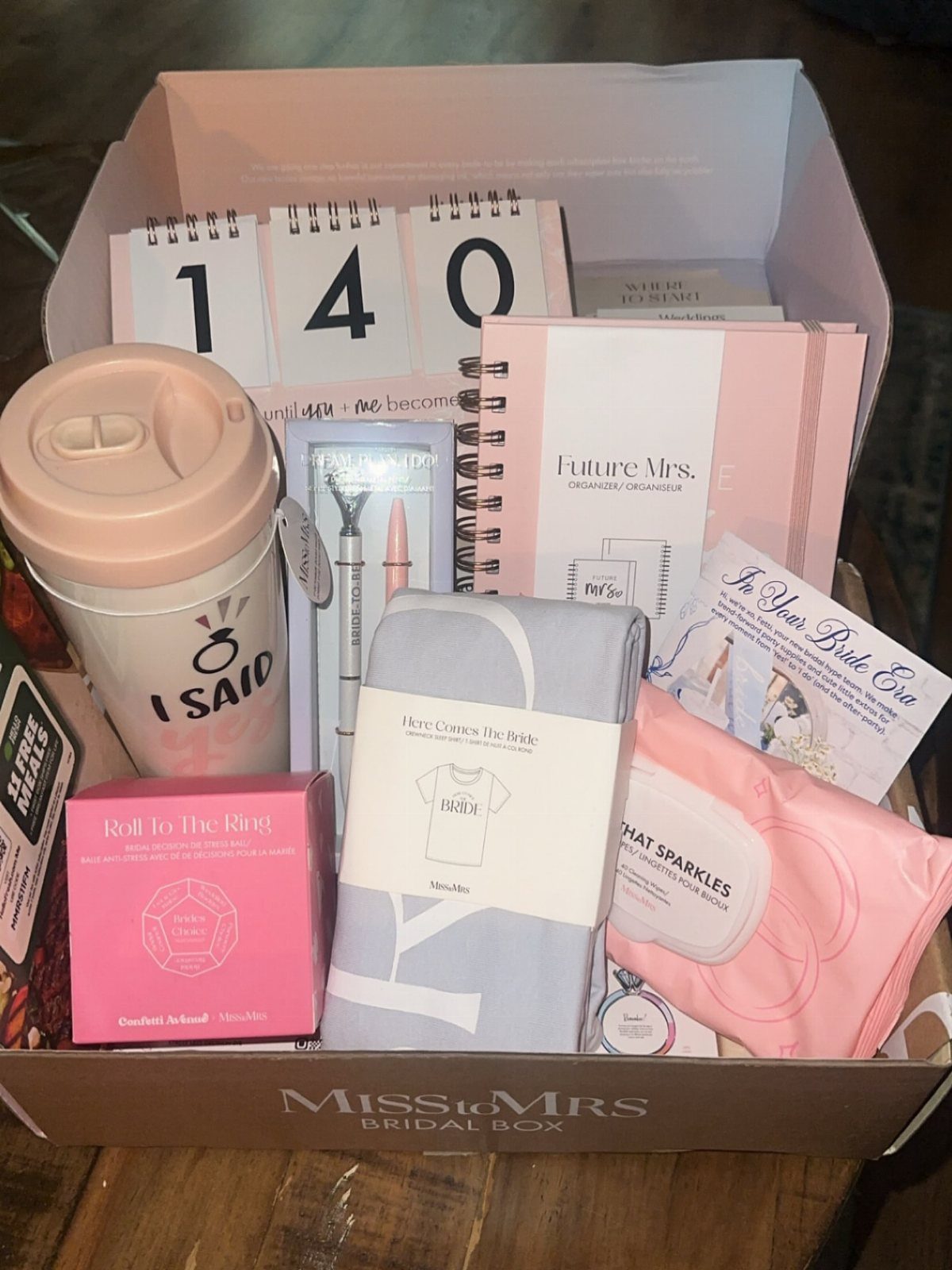 Bridal gift box filled with a travel mug, planner, and pink beauty products.