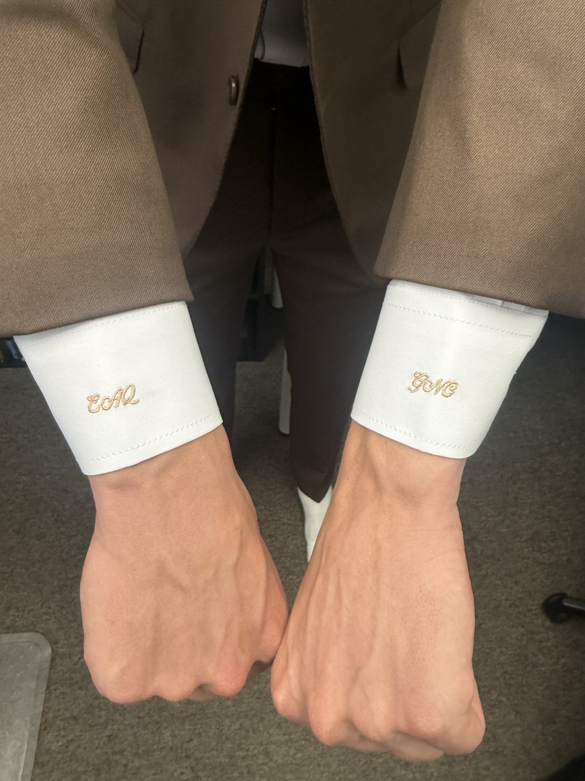 White dress shirt cuffs with gold embroidered initials under a tan suit jacket