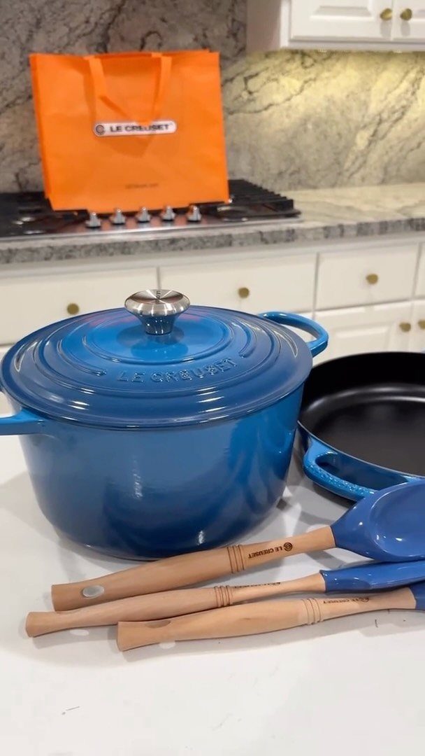 Blue Le Creuset round Dutch oven and skillet with utensils on white counter