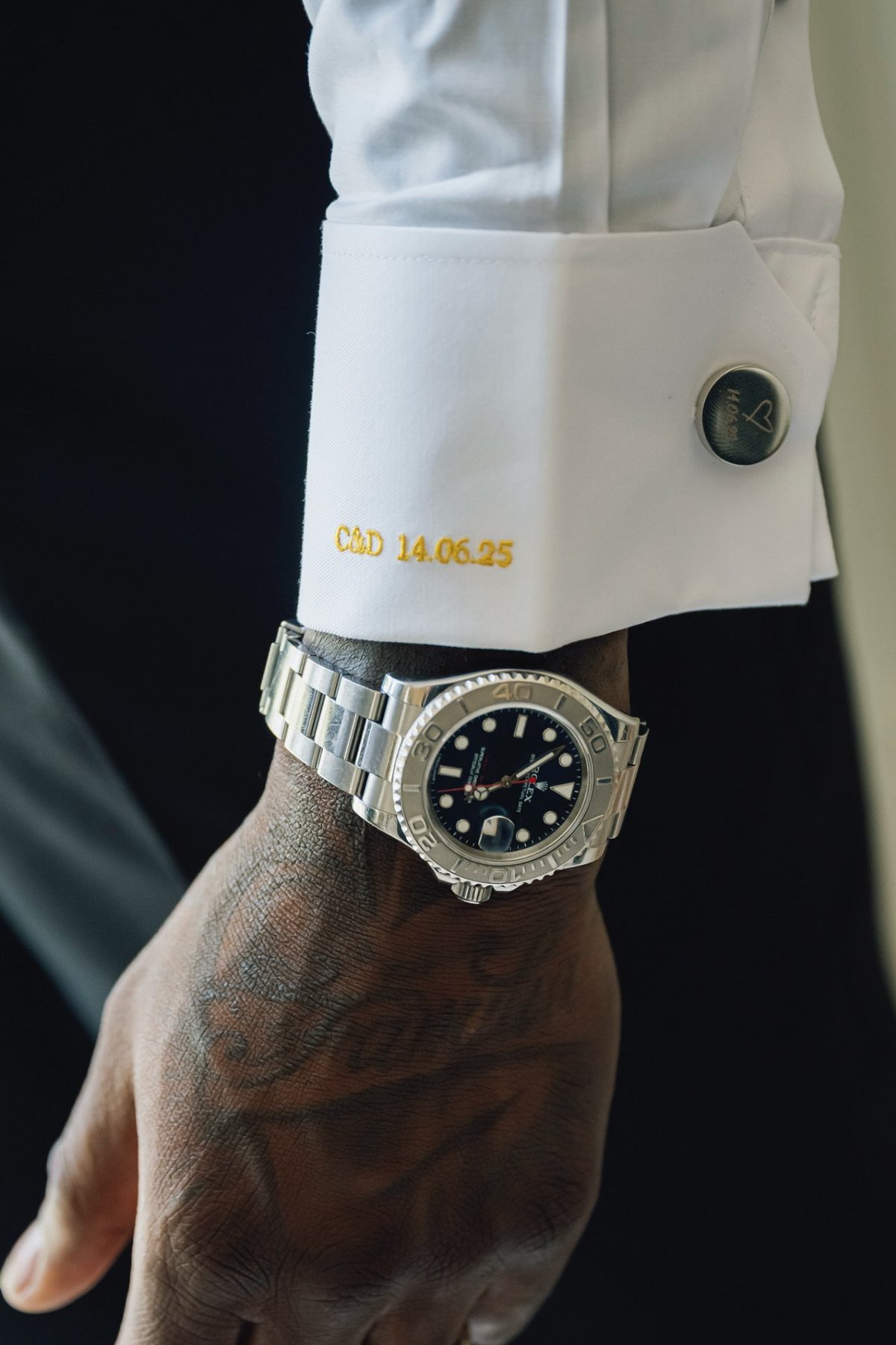 Silver luxury watch and dark cufflink on a white dress shirt cuff.