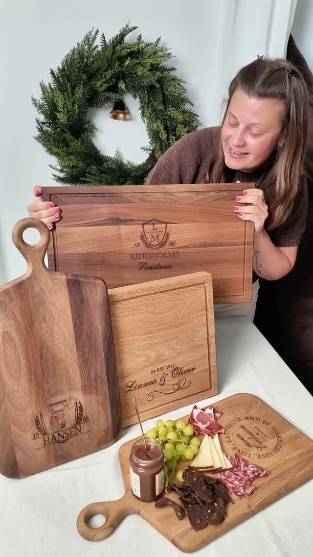 Woman holding and displaying several personalized engraved wooden cutting boards with a charcuterie spread.