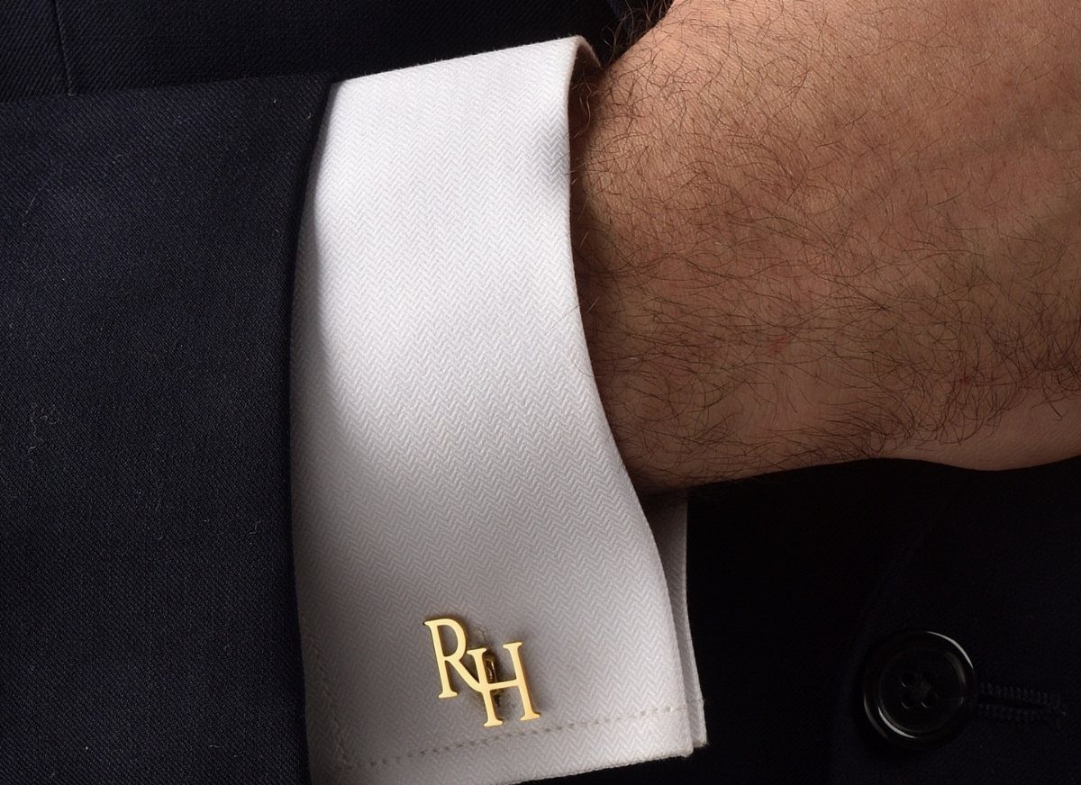Gold monogrammed RH cufflinks on a white dress shirt cuff and dark suit.