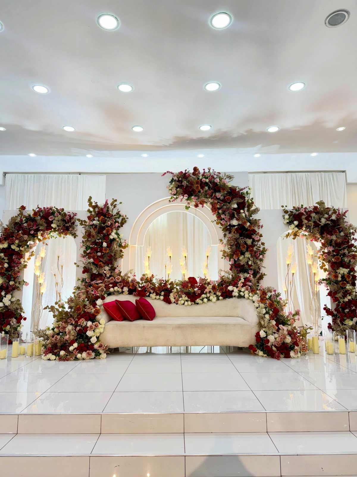 White curved sofa with red pillows surrounded by red and white floral arches.