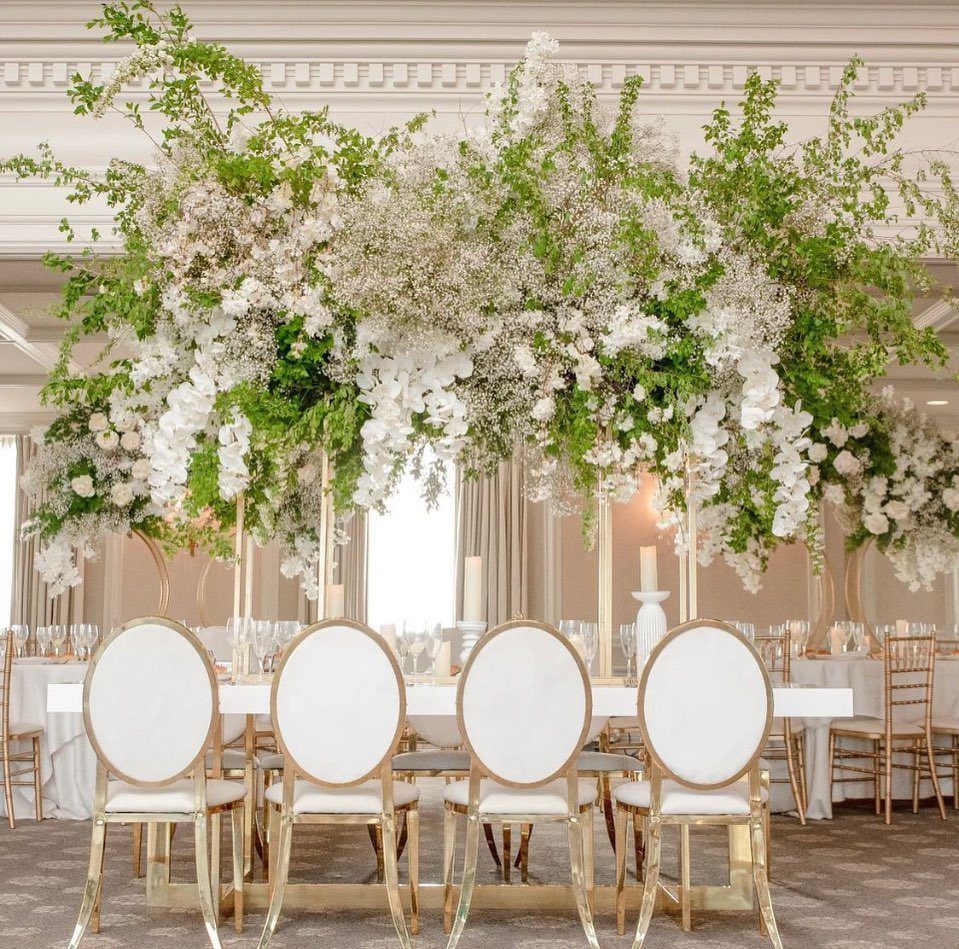Gold and white oval-back chairs at a wedding table under floral installations