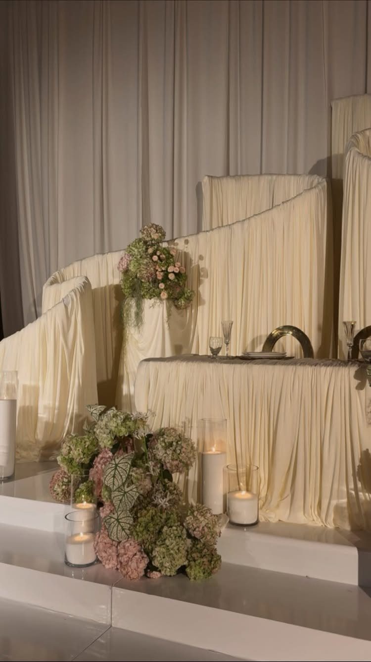 Small sweetheart table with cream fabric, floral arrangements, and white pillar candles.