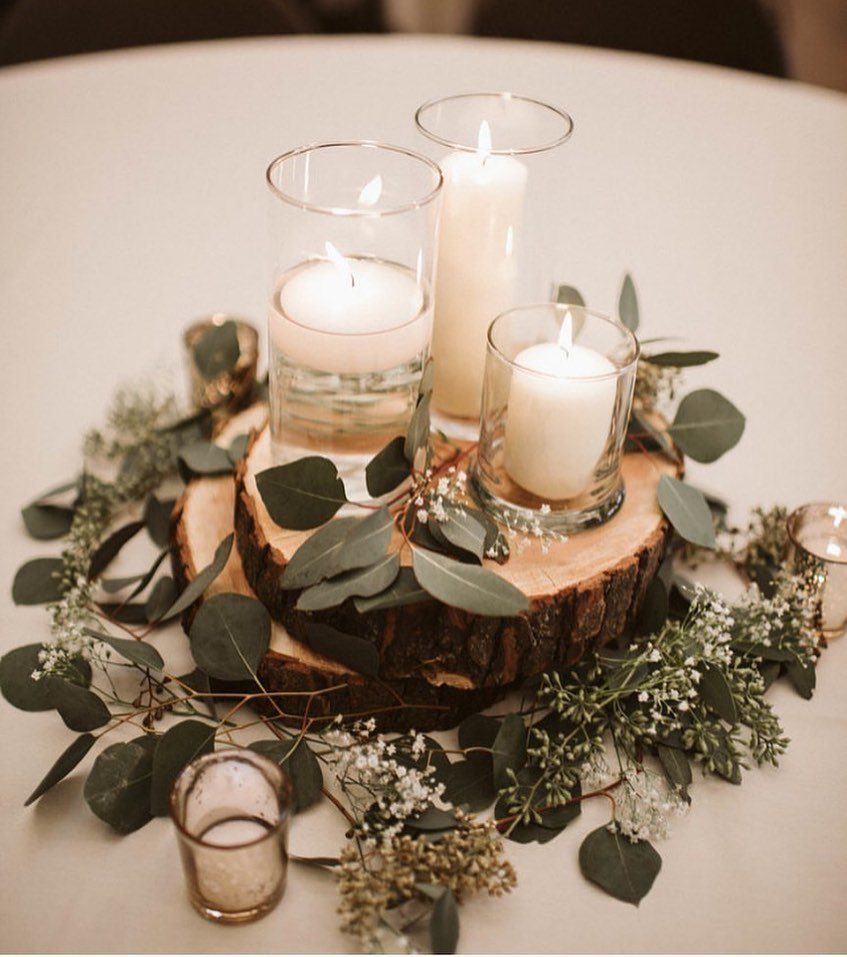White pillar candles in glass holders on a wooden slice with eucalyptus leaves