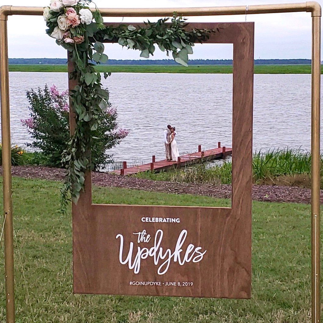 Wooden photo booth frame with floral accents standing outdoors by a lake
