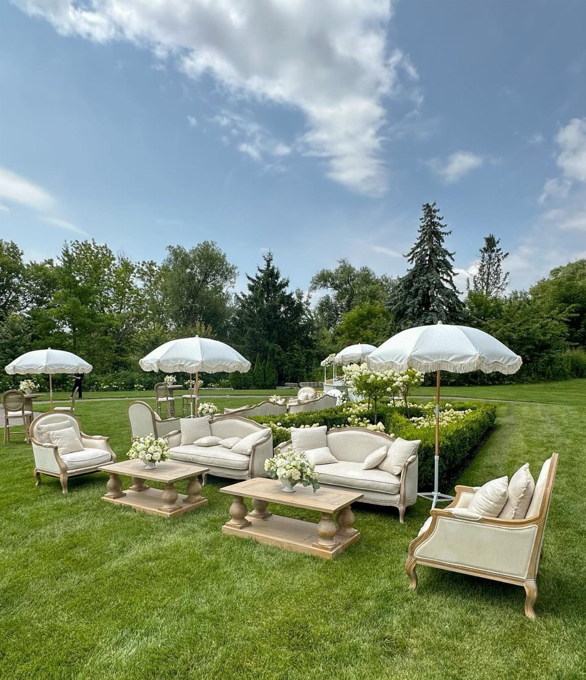 White upholstered outdoor lounge furniture with wooden tables and umbrellas on a lawn