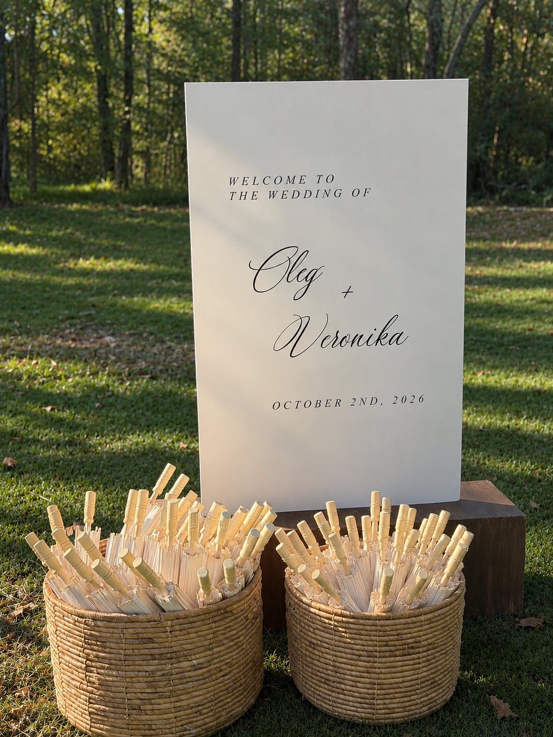 Wedding welcome sign and two woven baskets filled with bubble wands on grass.