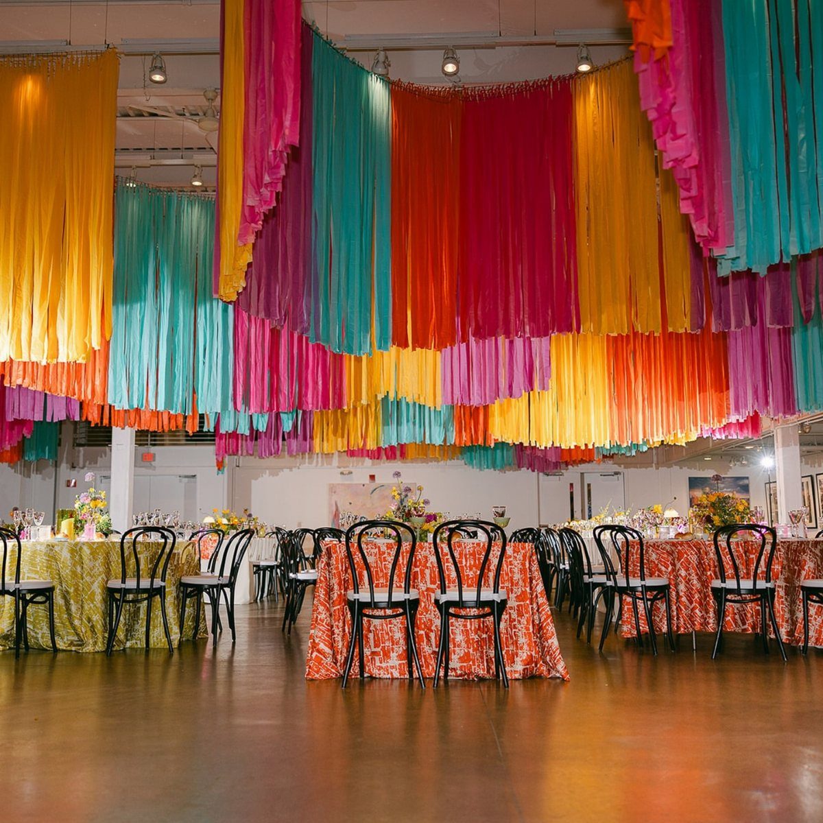 Colorful fabric streamers hanging from a ceiling over decorated event tables and chairs.