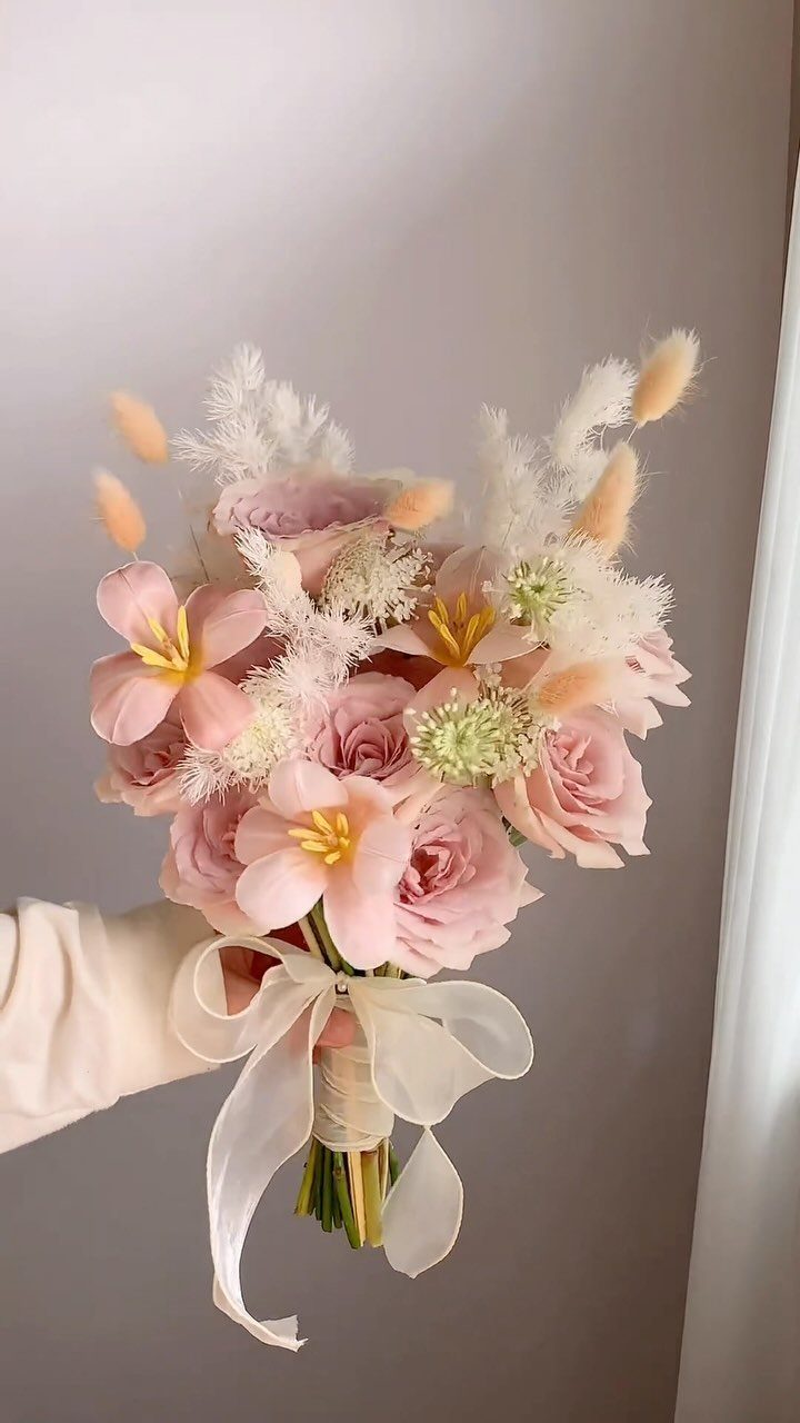 Bridal bouquet with pink roses and lilies tied with a white satin ribbon.