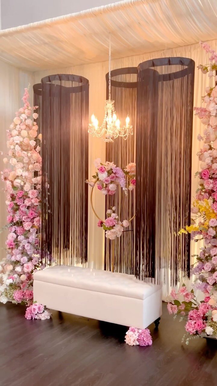 Wedding backdrop with shimmering curtains, floral hoop, white bench, and crystal chandelier.