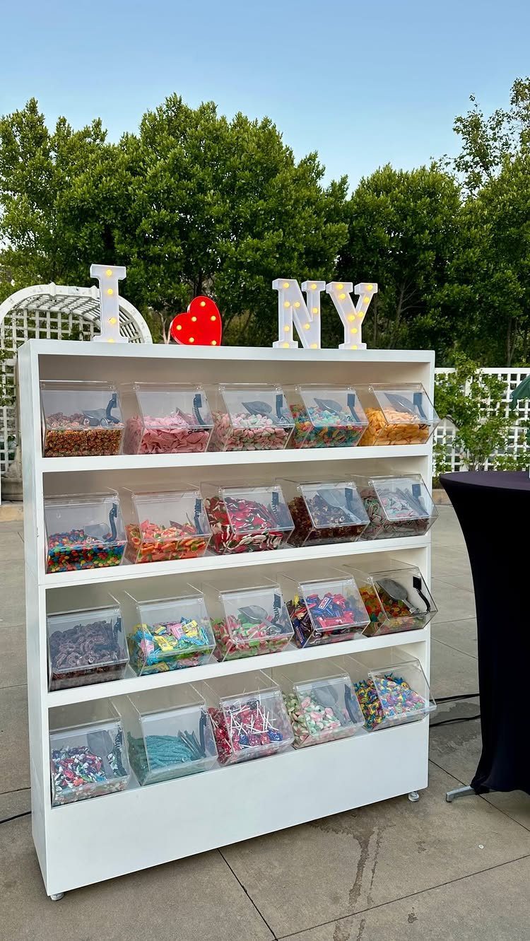 Candy bar with clear bins of colorful sweets on a white shelf outdoors.