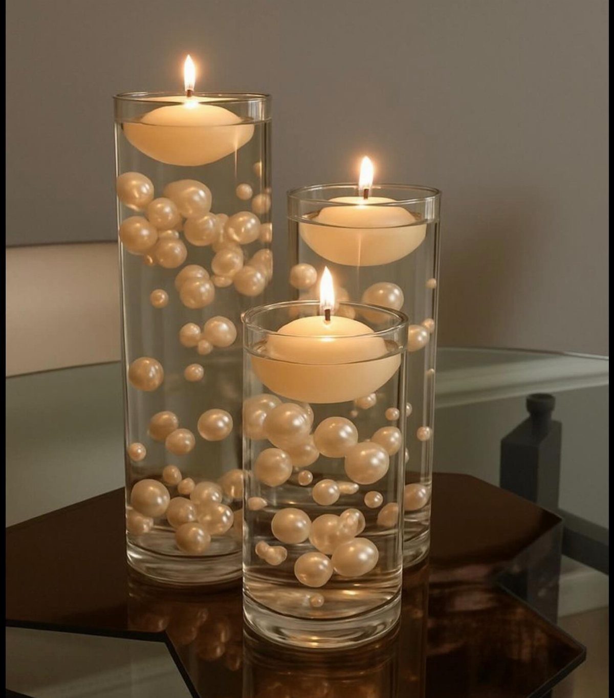 Three glass cylinder vases with floating candles and white pearls inside.