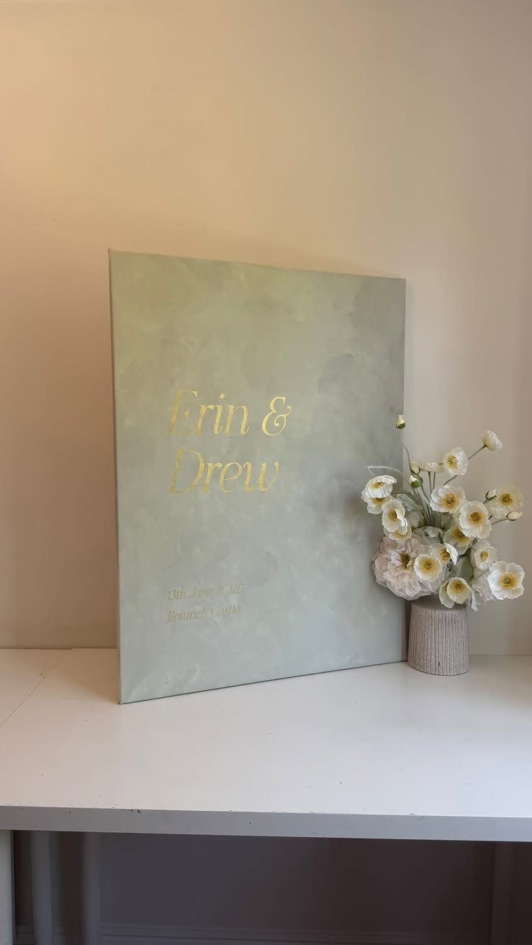 Light green canvas wedding sign with gold lettering and white flowers on table