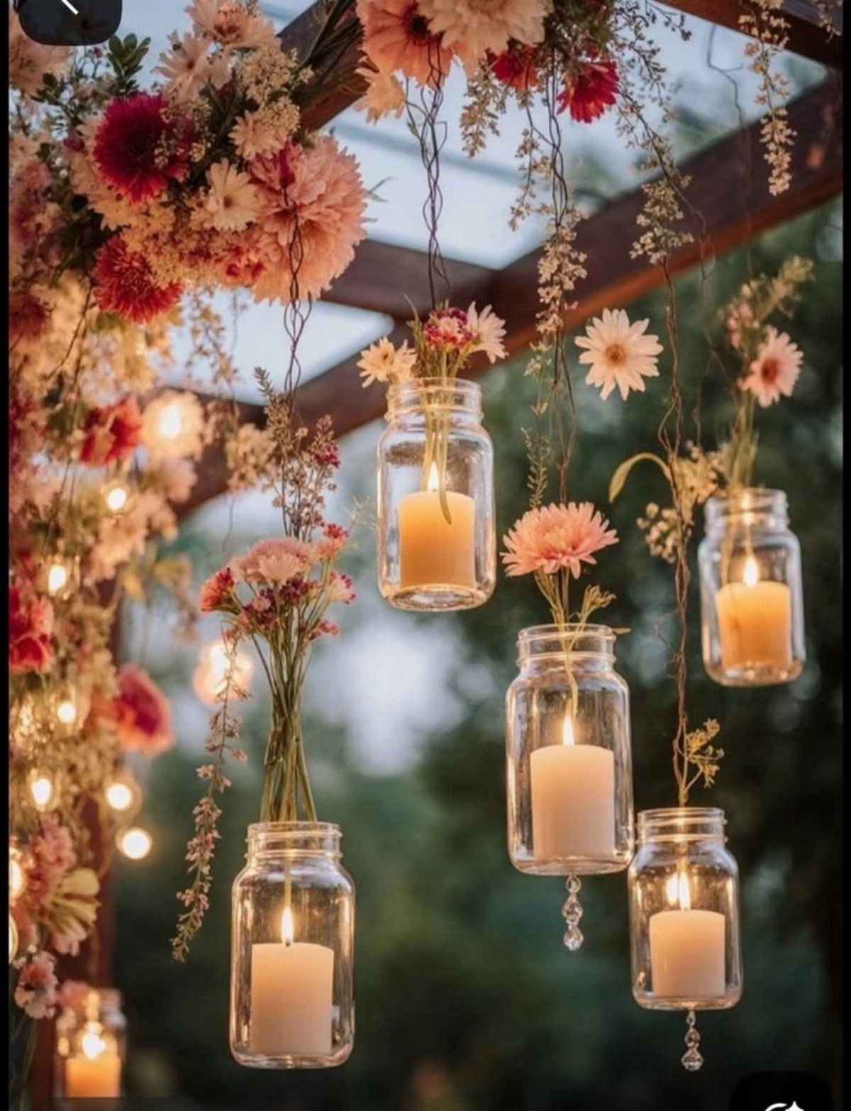 Hanging glass jar vases with candles and flowers under a floral pergola.