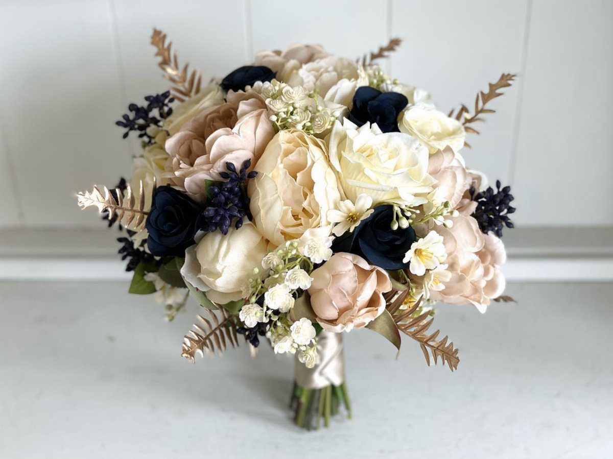 Bridal bouquet with navy blue, cream, and blush roses and gold metallic leaves.