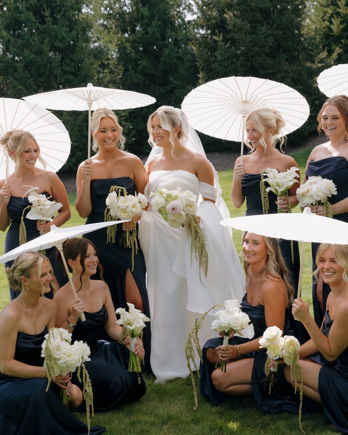 Bride in white gown surrounded by bridesmaids wearing navy blue strapless dresses.