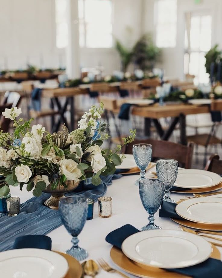 Wedding table setting with navy blue runner, gold chargers, and white floral centerpiece.