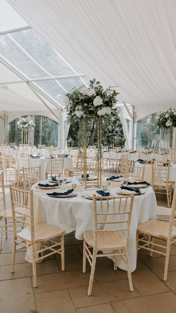 Wedding reception tables with white linens, navy blue napkins, and tall floral centerpieces.