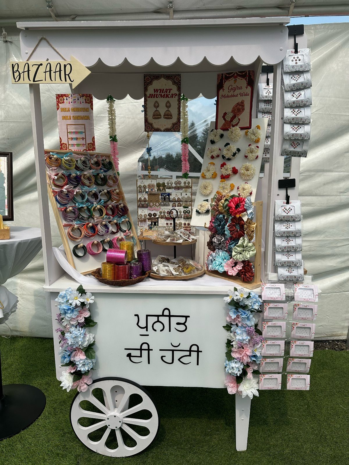 White wooden favor cart decorated with flowers and displaying jewelry and gift boxes.