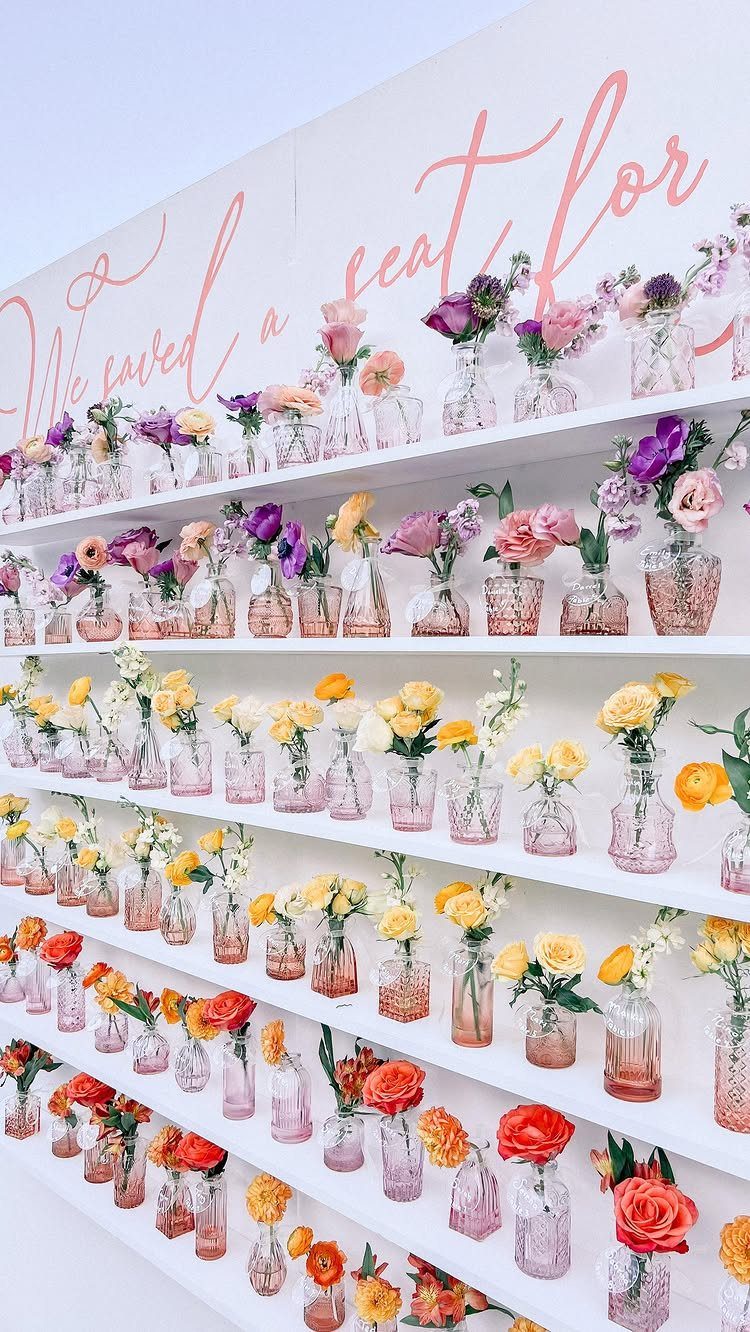 Small glass bottles with colorful flowers arranged on white shelves against a wall.