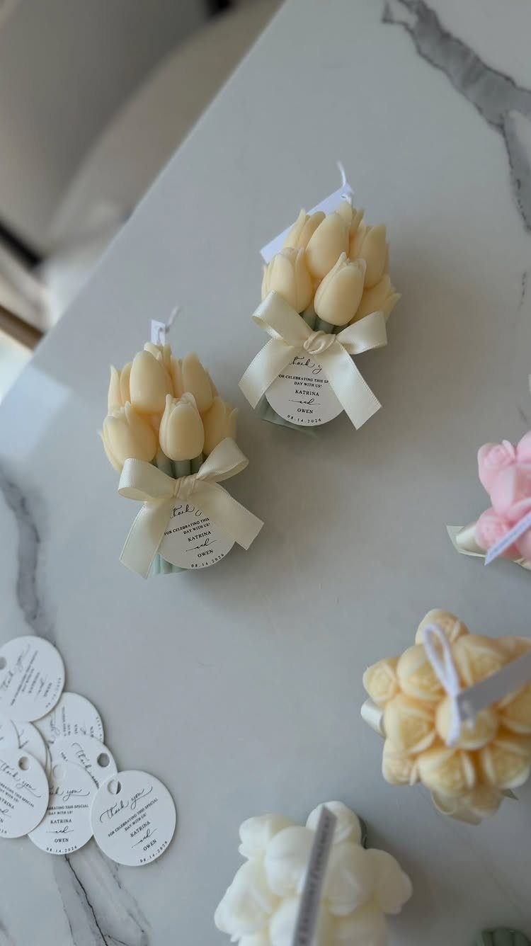 Tulip-shaped cream candles with white ribbons and tags on a marble surface.