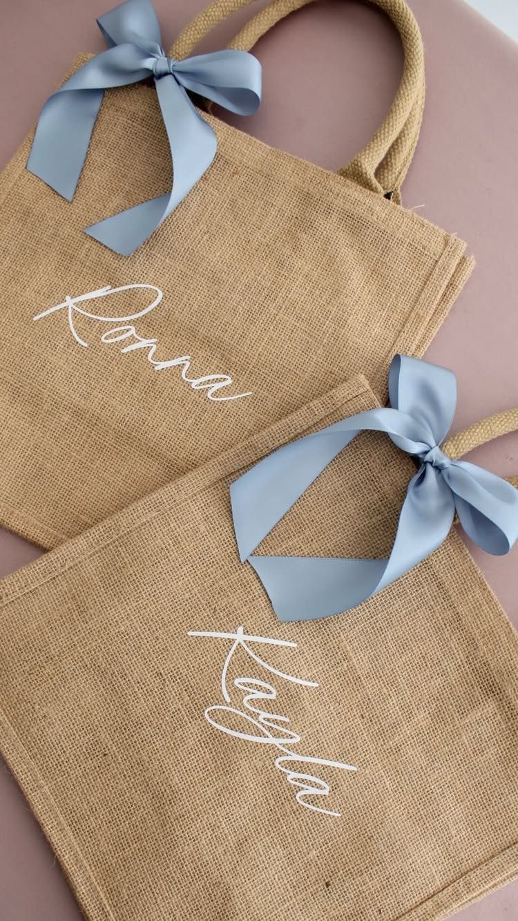 Burlap tote bags with light blue bows and white cursive names on them.
