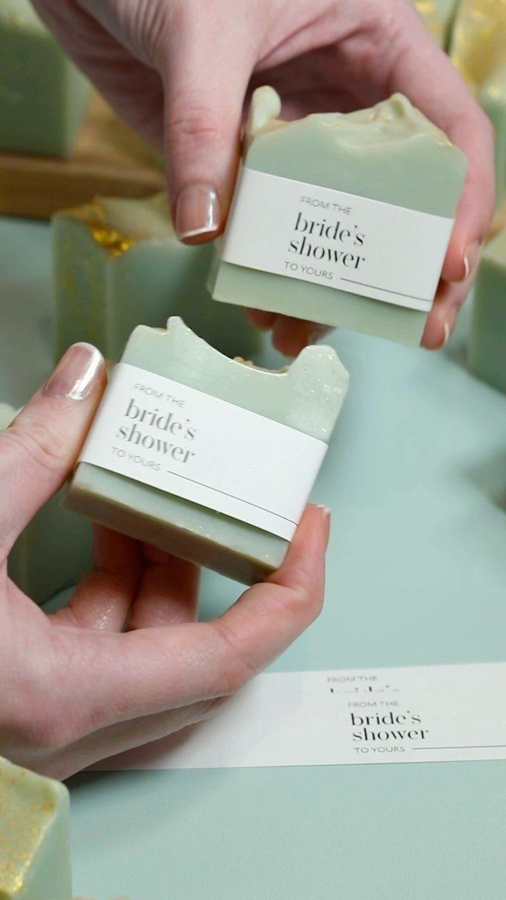 Light green artisan soap bars wrapped in white paper bands held by hands.