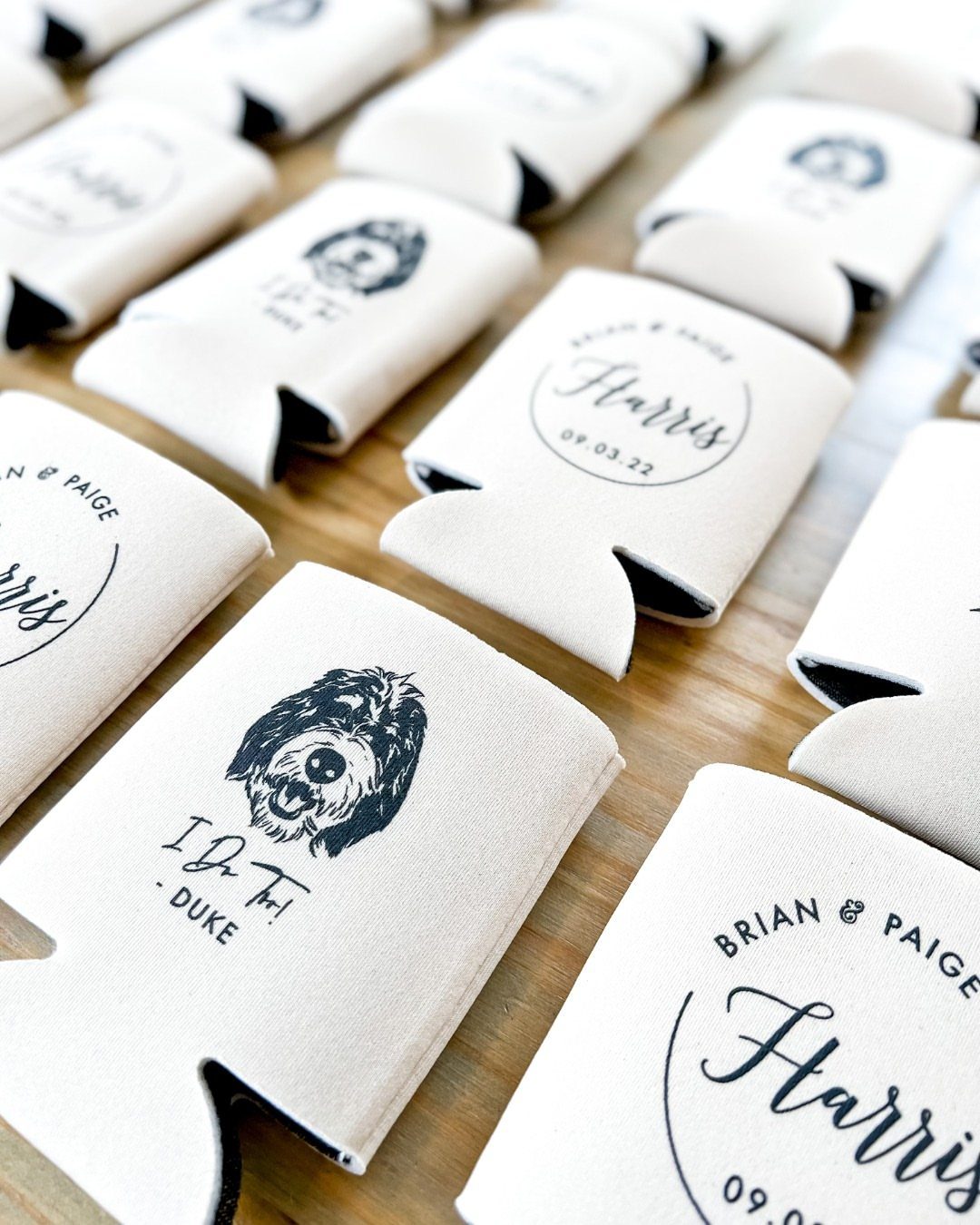 White custom koozies with dog illustrations and wedding names on a wooden table.