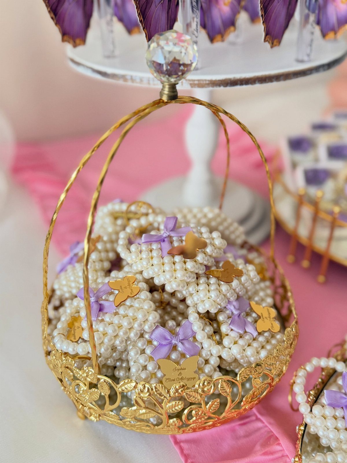 Pearl bracelets with butterfly charms filling a gold ornate metal basket on pink fabric.