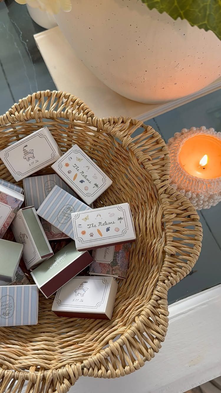 Small personalized matchboxes with illustrations resting in a woven wicker bowl.