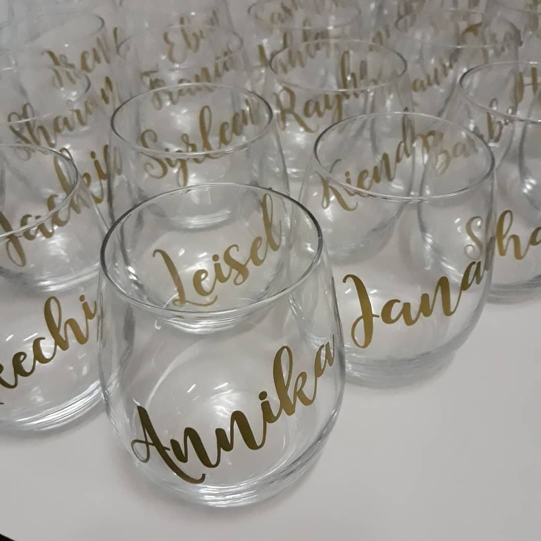 Stemless clear wine glasses with personalized names written in gold cursive calligraphy.