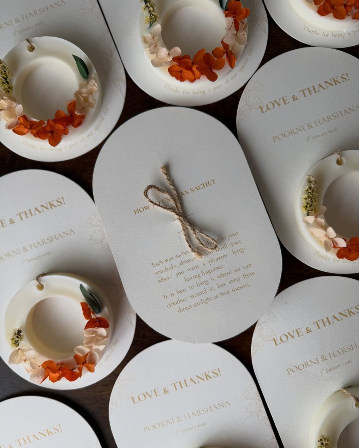 White wax sachets with dried flowers on oval cards with gold wedding text.