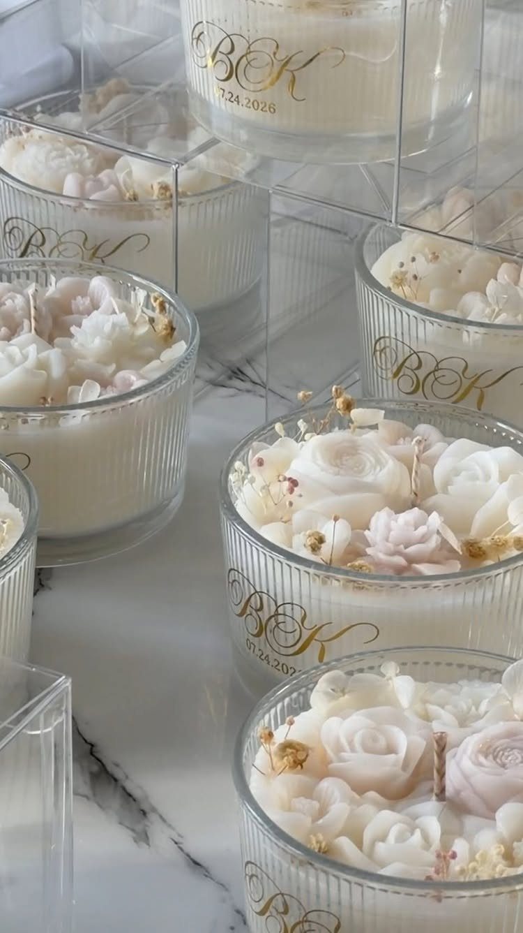 White scented candles with wax roses and gold lettering on marble surface