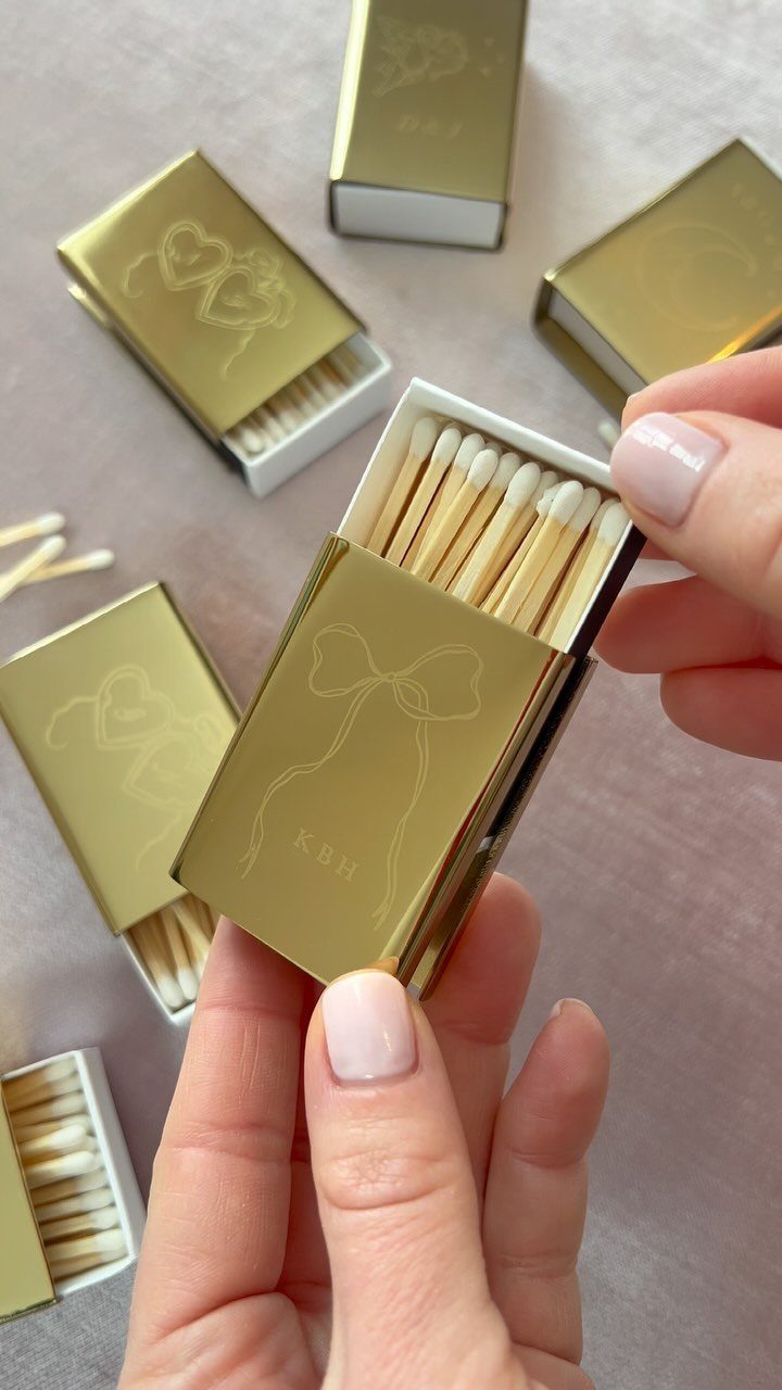 Gold custom matchboxes with a bow design held in a person's hands.