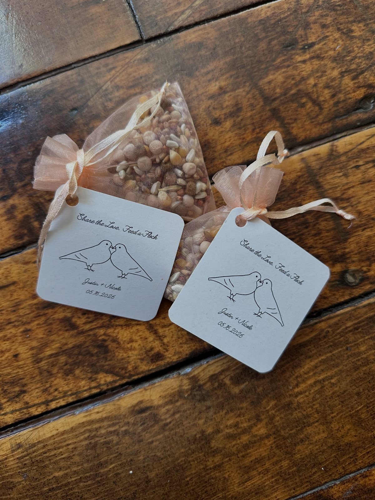 Two birdseed favor bags with peach ribbons and bird-themed tags on wood.