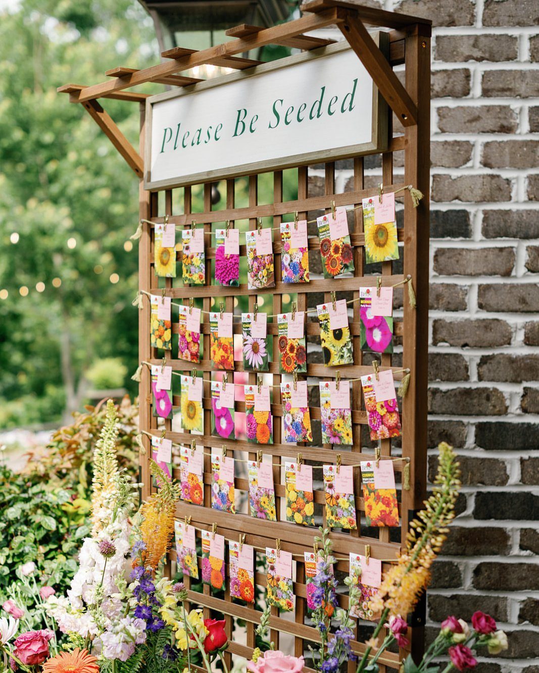 Seed packets with flower illustrations hanging on a wooden trellis for wedding guests.