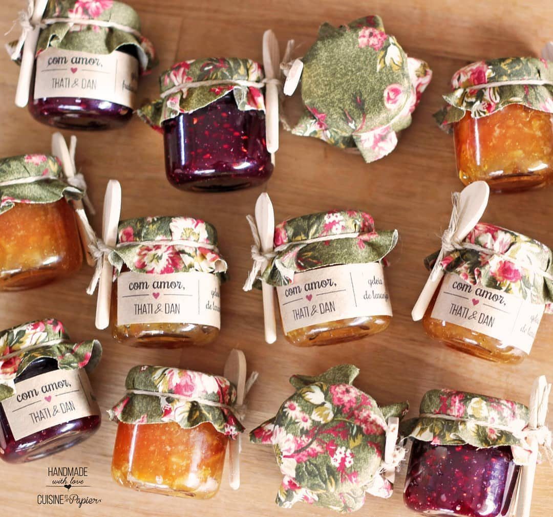 Small jars of red and orange jam with floral fabric lids and wooden spoons.