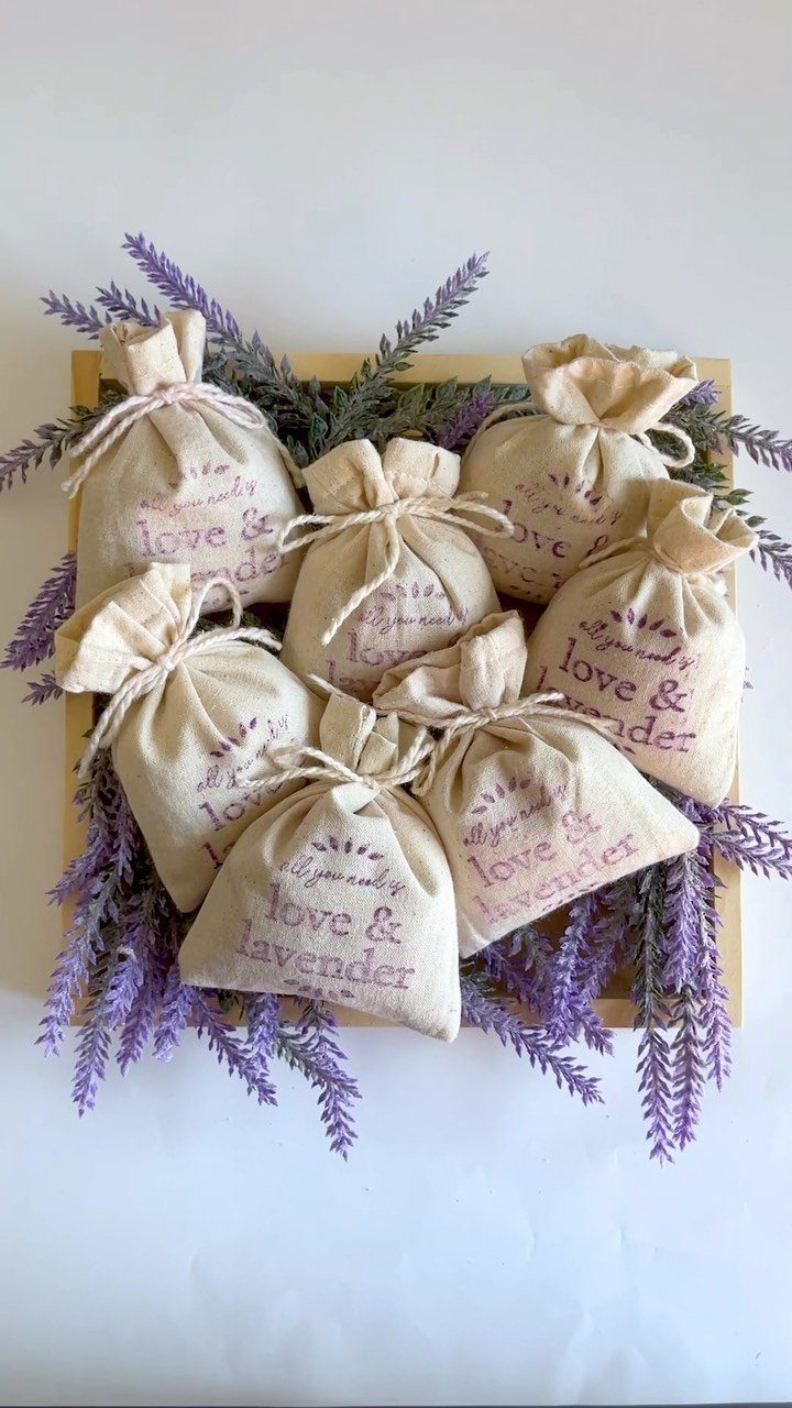 Cream fabric lavender sachets with purple text arranged in a wooden tray with lavender.