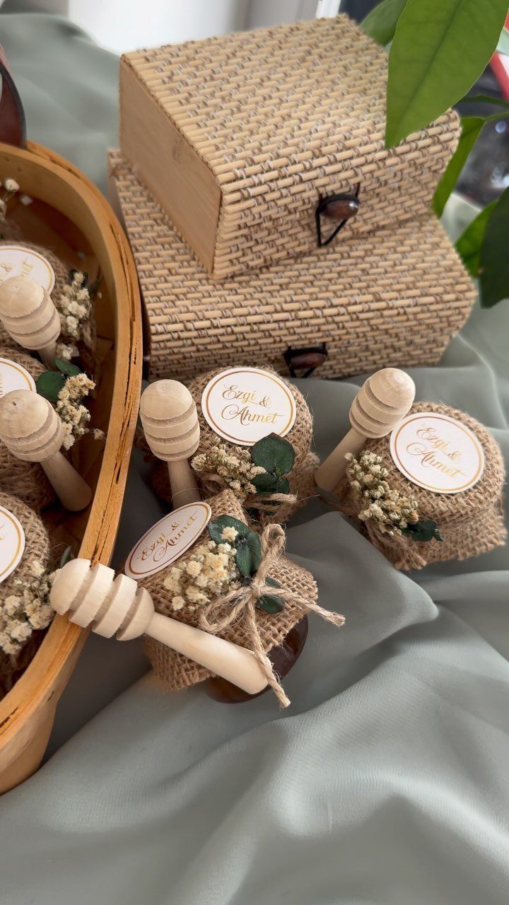 Small honey jars with burlap lids, wooden dippers, and personalized labels for weddings.