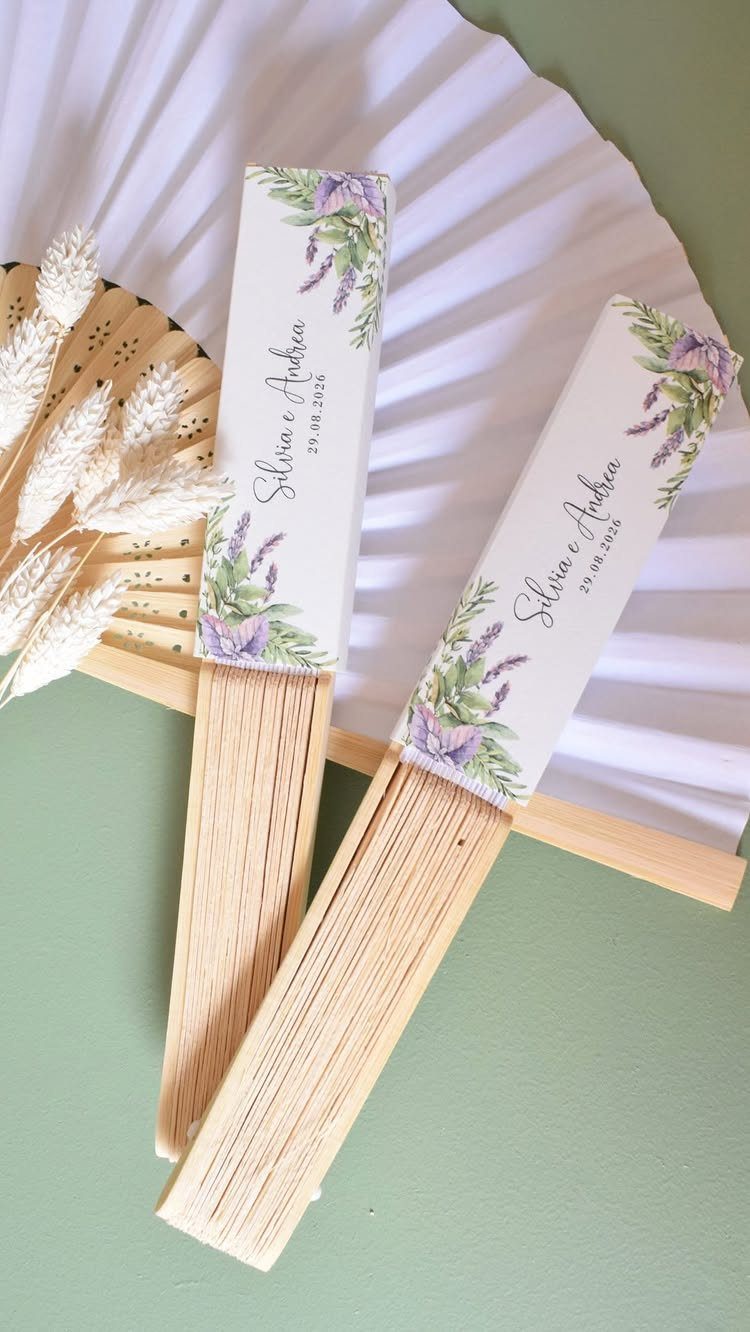 Two closed folding paper fans with lavender designs and names on green background