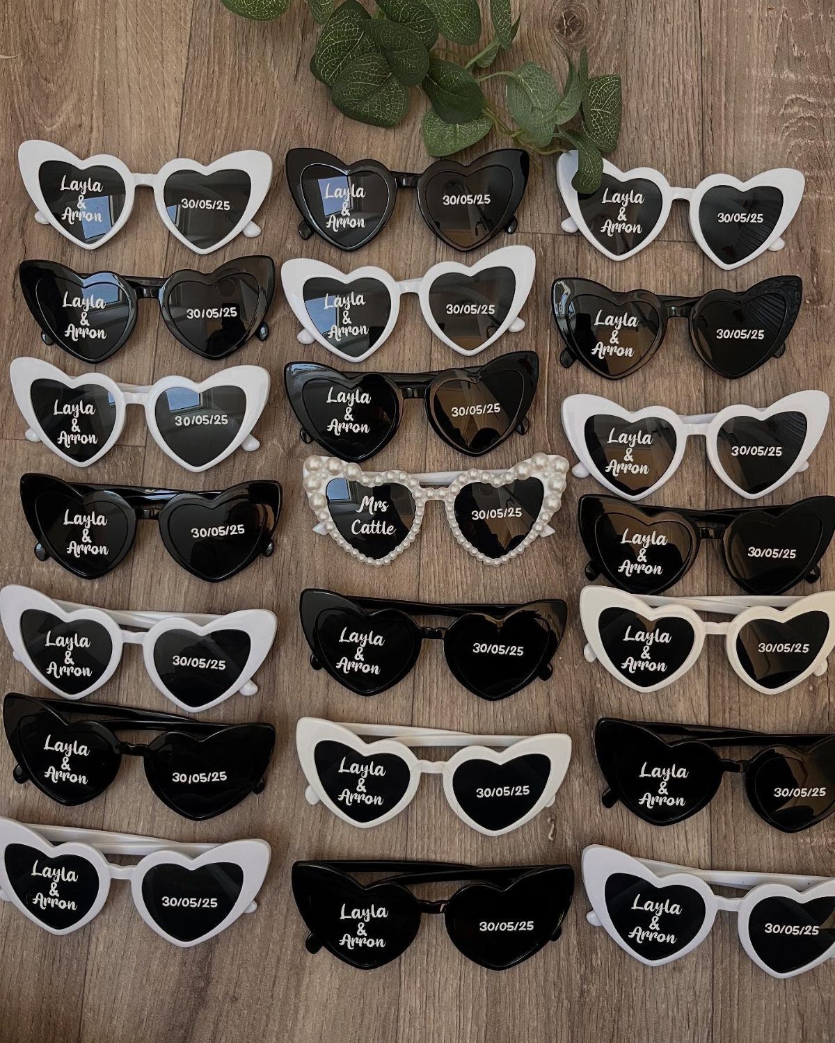 Heart-shaped black and white sunglasses with personalized text on a wooden background.