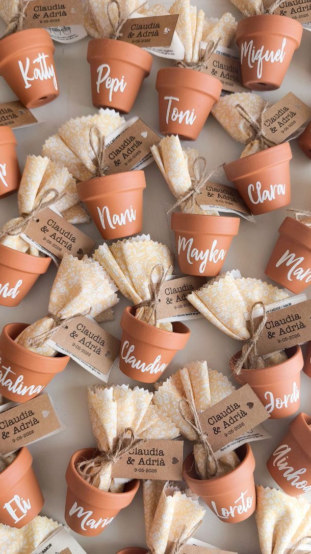 Small terracotta pots with handwritten names and gift tags for a wedding event.