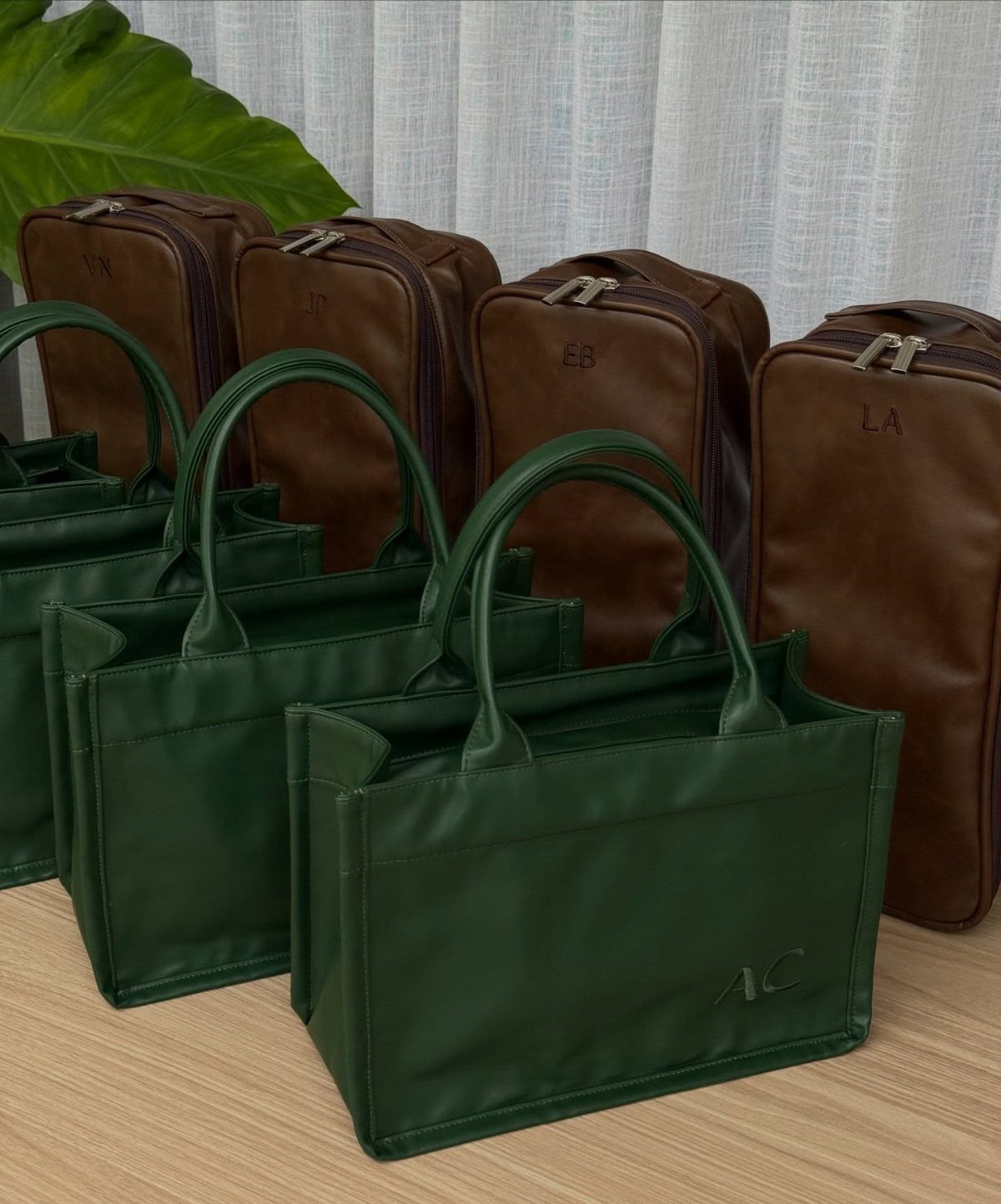 Leather travel bags in green and brown with embossed initials on wooden surface