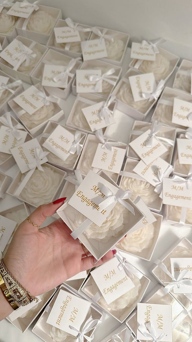White flower-shaped candles in small gift boxes with engagement tags and white ribbons.