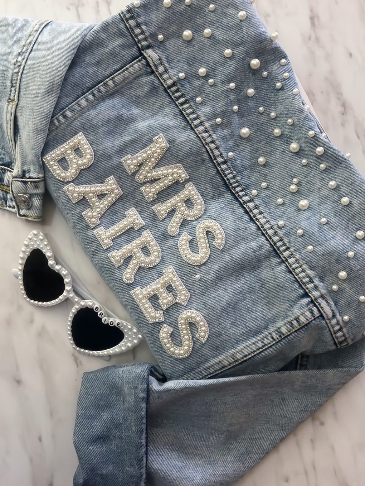 Denim jacket with Mrs Bairds spelled in pearls and heart-shaped pearl sunglasses.