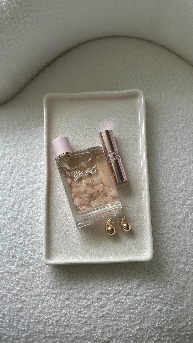 Perfume bottle labeled Bride with gold earrings on a white ceramic tray